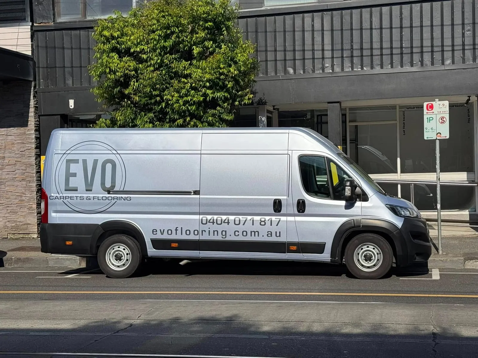 The silver Evo Carpets & Flooring van, signwritten with the logo, phone number and website, parked on a city street
